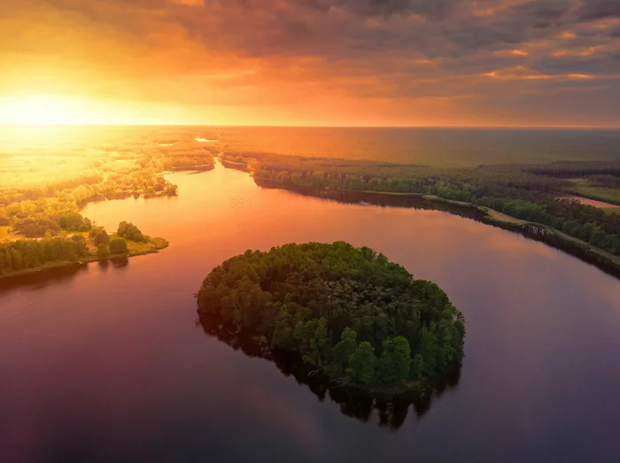 Luftaufnahme eines Sees mit bewaldeter Insel im Abendlicht